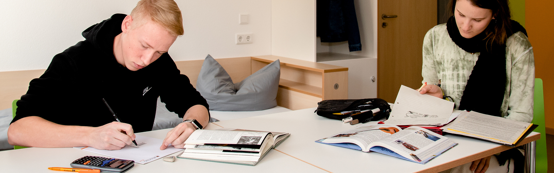 Junger Mann und junge Frau lernen gemeinsam an einem Tisch mit Büchern und Notizen.