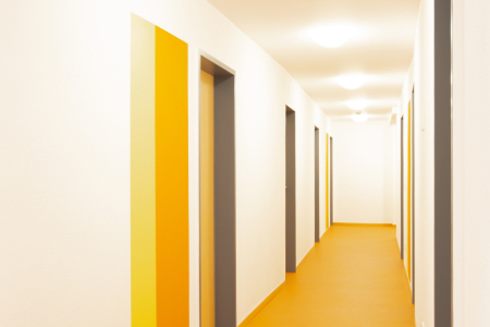 Langer, heller Flur mit mehreren Türen und orangefarbenem Bodenbelag.