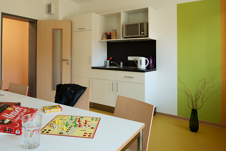Gemeinschaftsraum mit Tisch, Brettspiel und kleiner Küchenzeile.