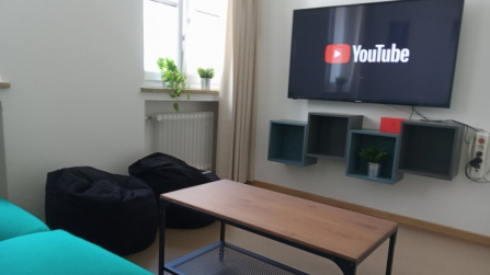Gemütlicher Aufenthaltsraum mit Sofa, Sitzsäcken, Couchtisch und Fernseher mit YouTube-Anzeige.